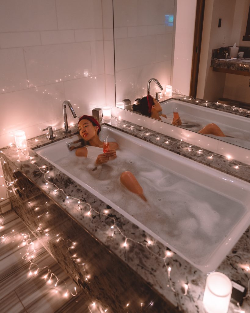 Woman taking bubble bath with candles and champagne