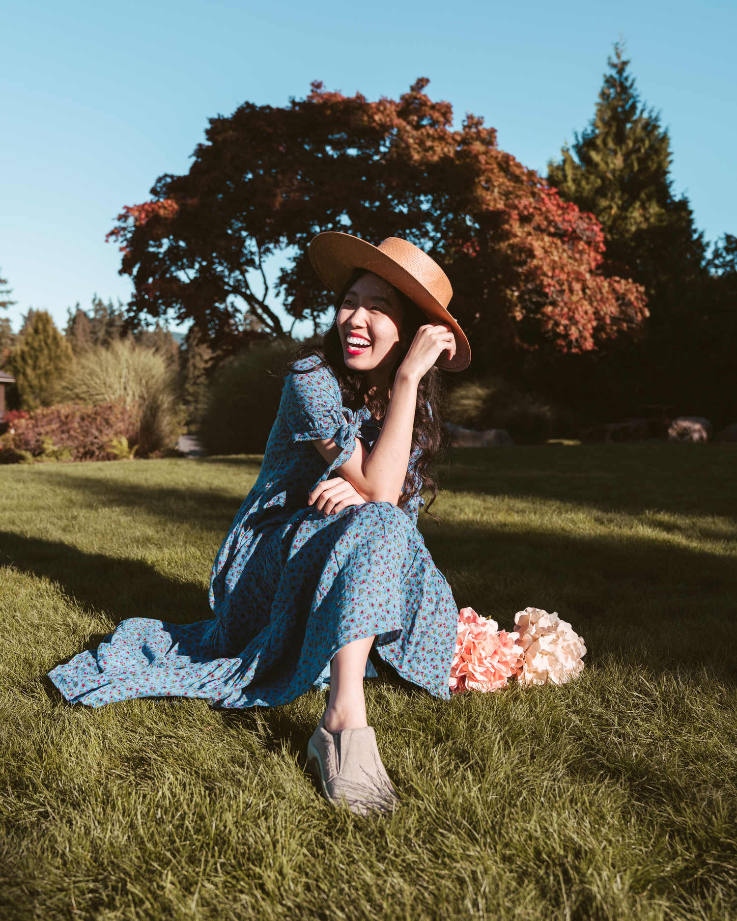 Girl laughing while sitting in the grass with autumn tree behind her