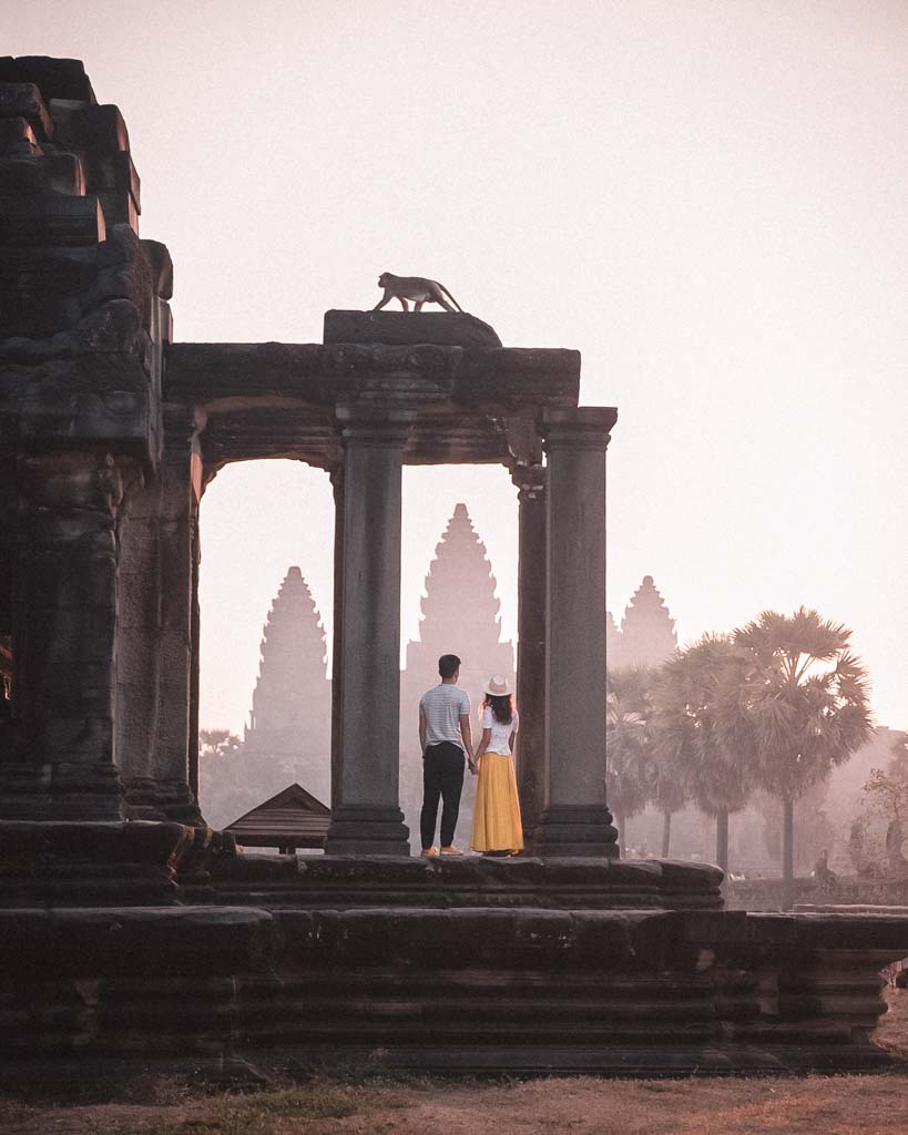 image of a couple on the steps of a ruin looking towards angkor wat. Monkey is above them making for an even more interesting image