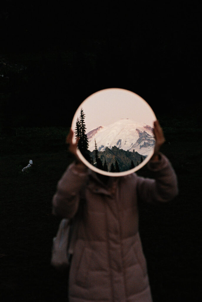 image of a girl holding up a mirror with mount rainier reflection in the mirror