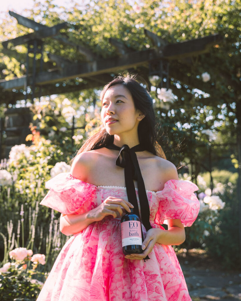 image of girl in pink dress in front of green trees holding a bottle of shampoo